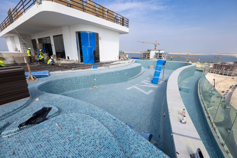 Beach Walk Residence A rooftop pool under construction, featuring blue mosaic tiles and workers in safety vests, with a city view.